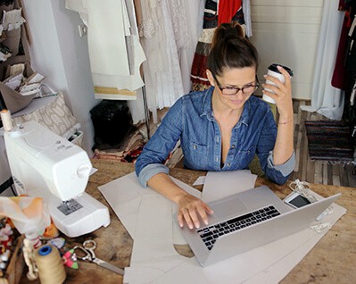 Creative business owner reviewing laptop holding a cup of coffee